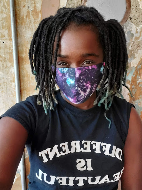 Portrait of Chardae Jones behind an unfinished wall while wearing a galaxy print face mask. 
